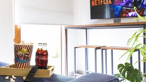 En hyggelig stue med et TV på væggen, der viser Netflix, et træbord med popcorn og sodavandsflasker, og en behagelig sofa.