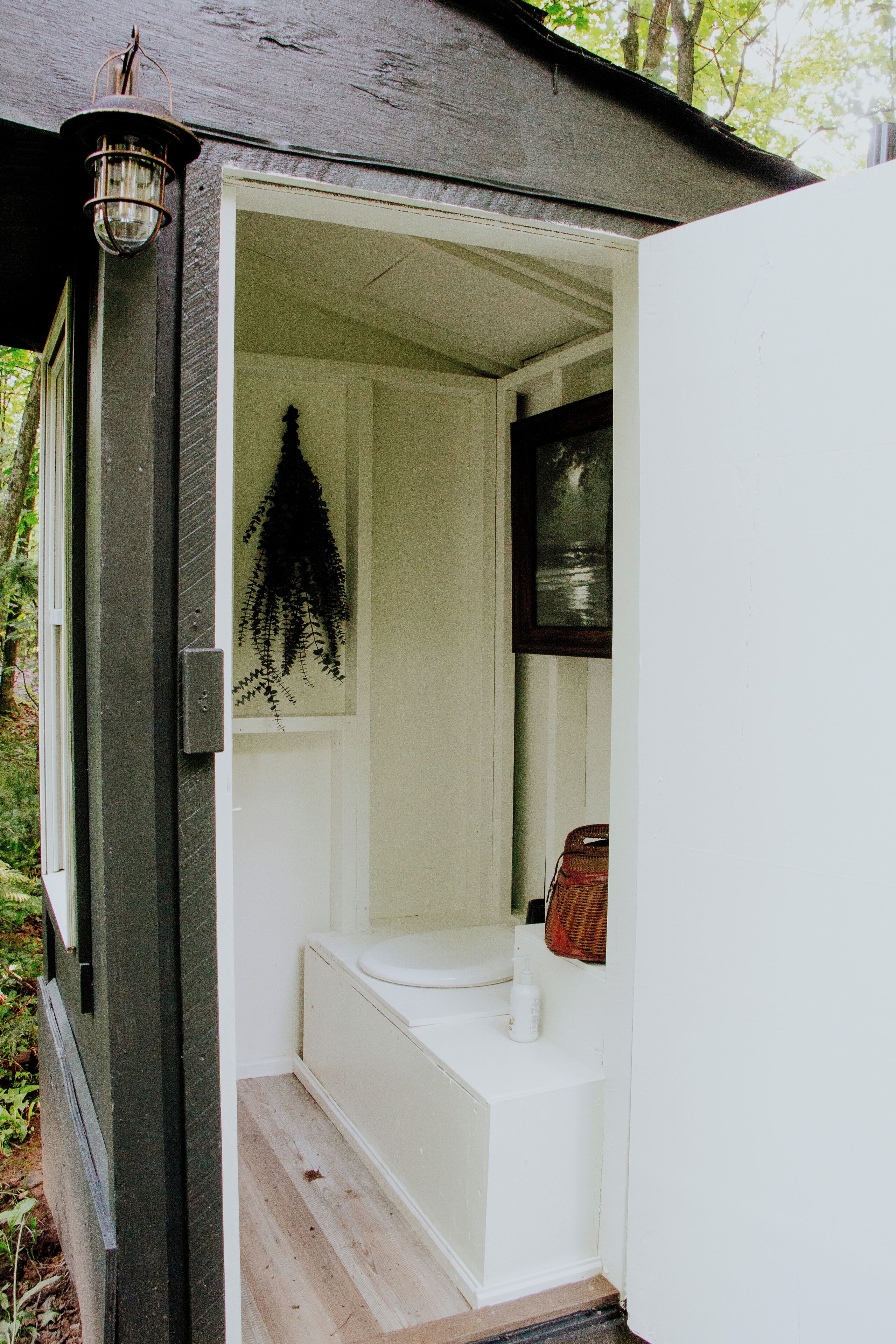 Een compacte, afgesloten badkamer met een houten vloer, een witte wastafel en een hangplant.