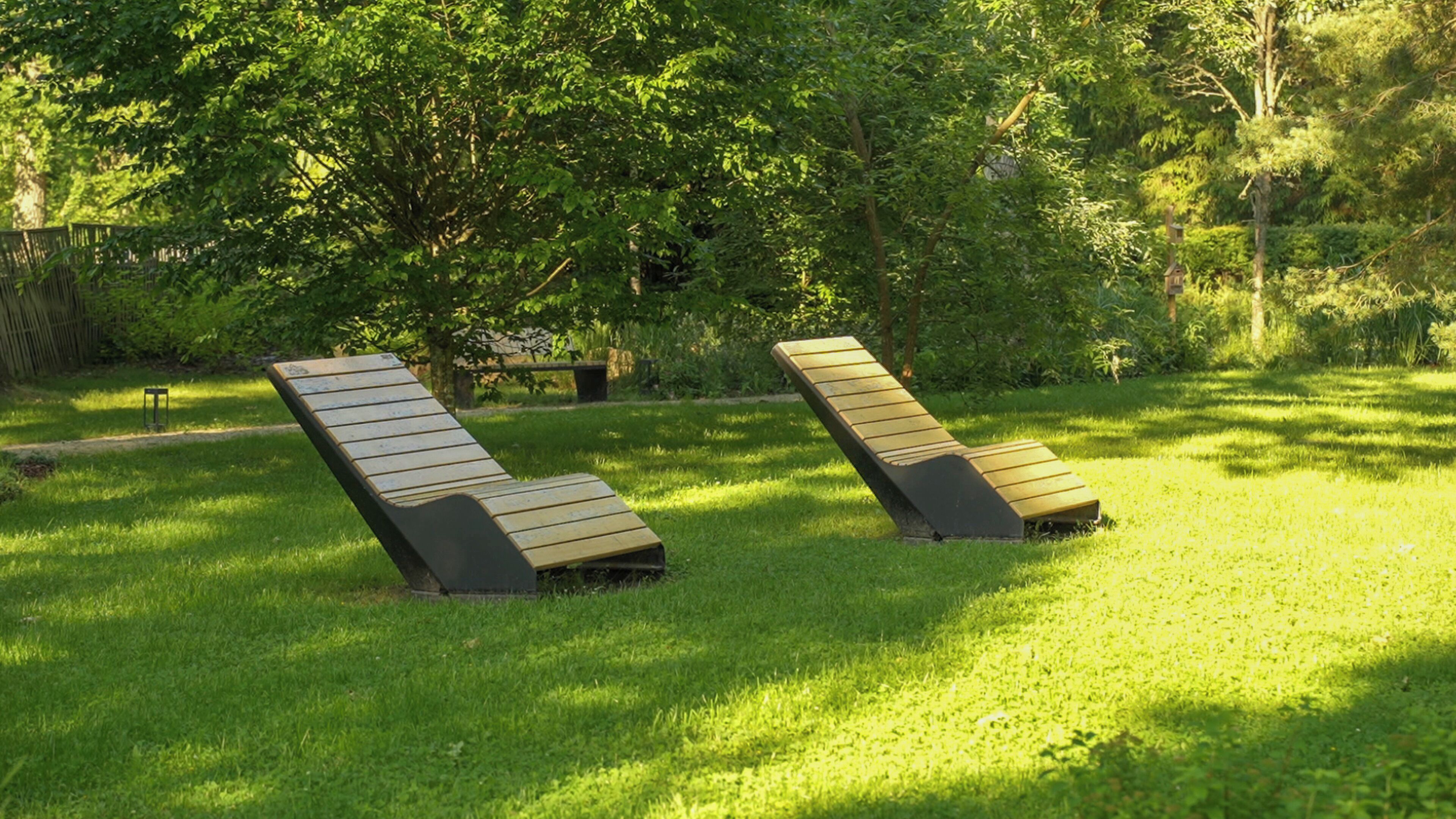Two reclining lounge chairs in a grassy outdoor area with trees in the background.