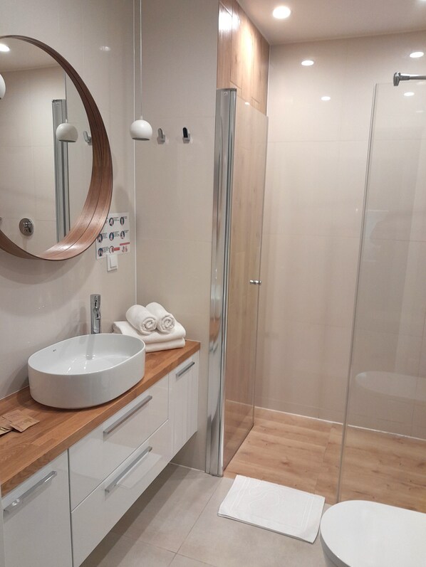 Une salle de bain moderne avec un miroir rond, un lavabo blanc et une cabine de douche en verre.