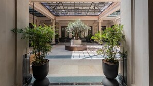 A spacious indoor courtyard with a central circular planter, flanked by potted plants, and a glass ceiling above. - Casa Vel Apartment by Wonderful Italy (Turin)