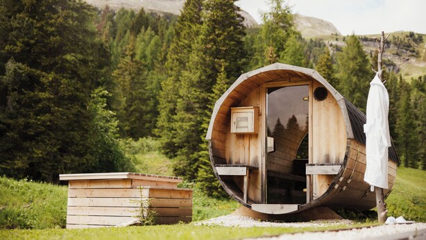 Una cabaña de madera con un diseño circular, una pequeña estructura de madera a su lado, y una persona parada afuera.