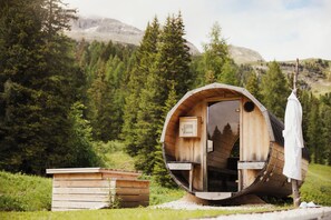 A wooden cabin with a circular design, a small wooden structure beside it, and a person standing outside. - Sports and Nature Hotel Boè (Livinallongo del Col di Lana)