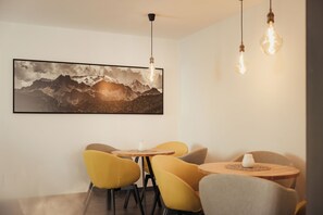 Un comedor con una mesa redonda, sillas amarillas y un cuadro de un paisaje montañoso en la pared.