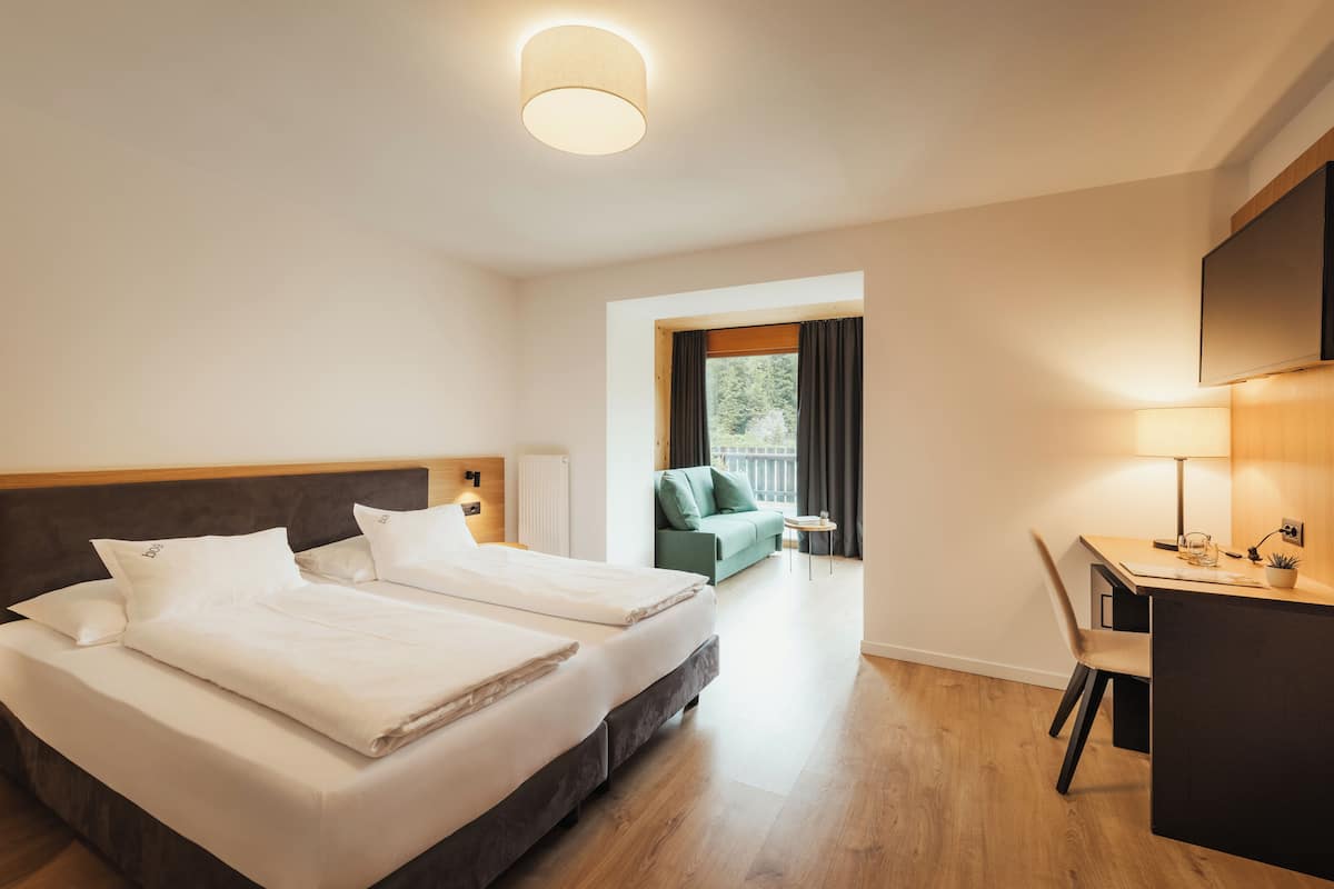 Hotellihuone, jossa on sänky, työpöytä, tuoli, televisio ja ikkuna, jossa on verhot.