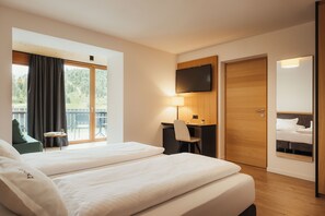Habitación de hotel con dos camas, un escritorio, una silla, un televisor y un balcón con cortinas.