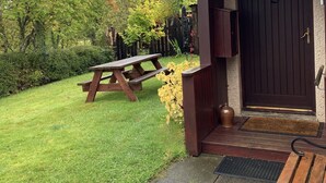 A house with a dark wooden door, a small porch, and a picnic table in the yard. - Smithy Cottage Licence AS00607 (Strathdon)