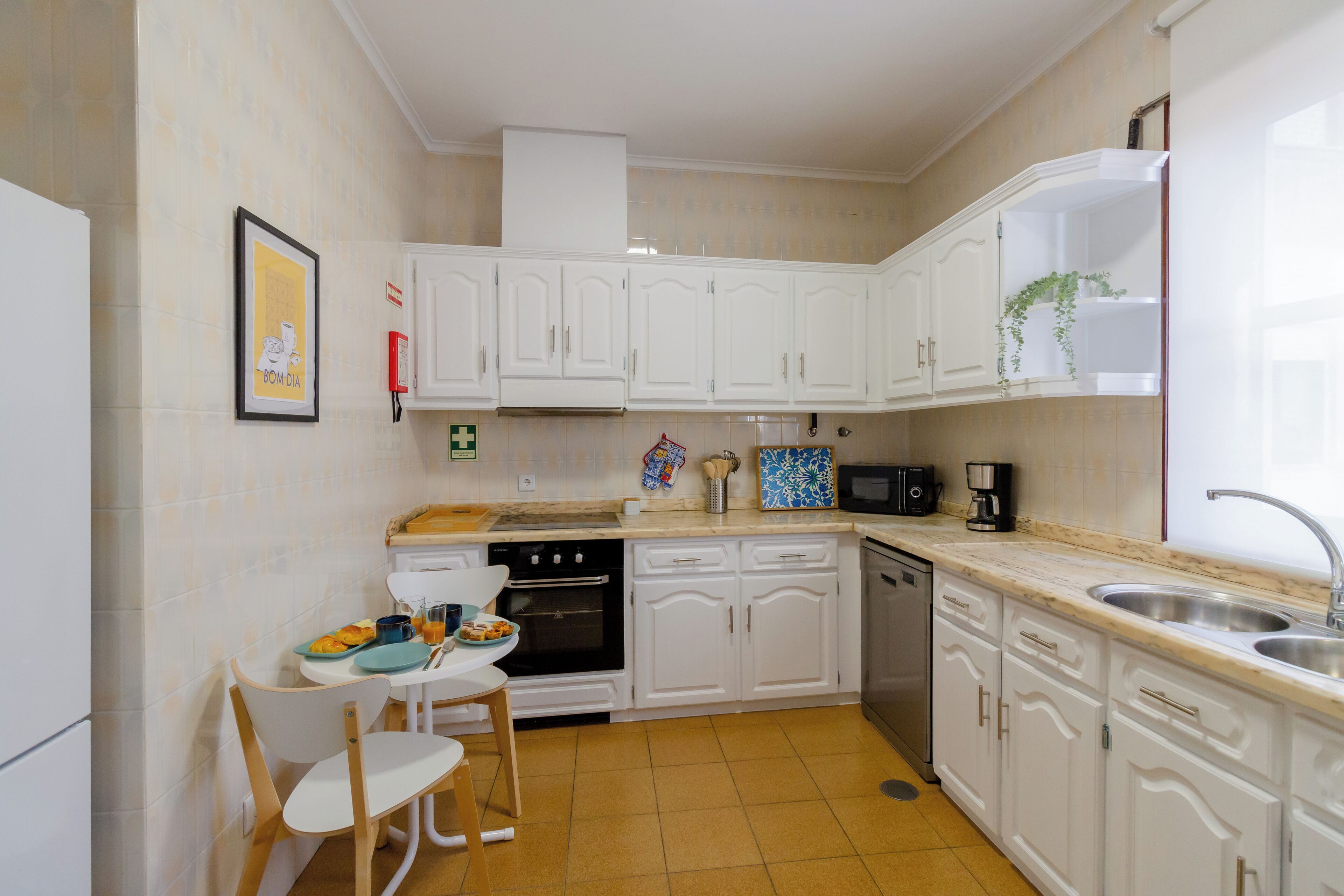 Una cucina con mobili bianchi, un forno a microonde, un lavandino e un'area pranzo con tavolo e sedie.
