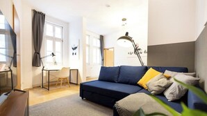 Una sala de estar moderna con un sofá azul oscuro, un escritorio pequeño y una lámpara.