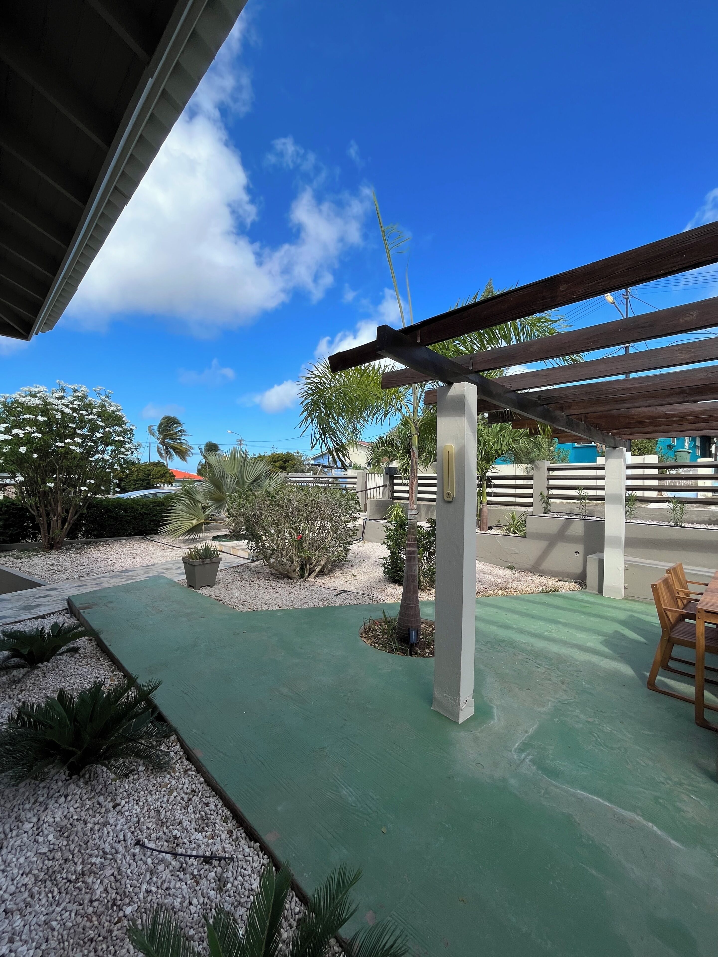 An outdoor patio area with a pergola, seating, and a view of a residential neighborhood.