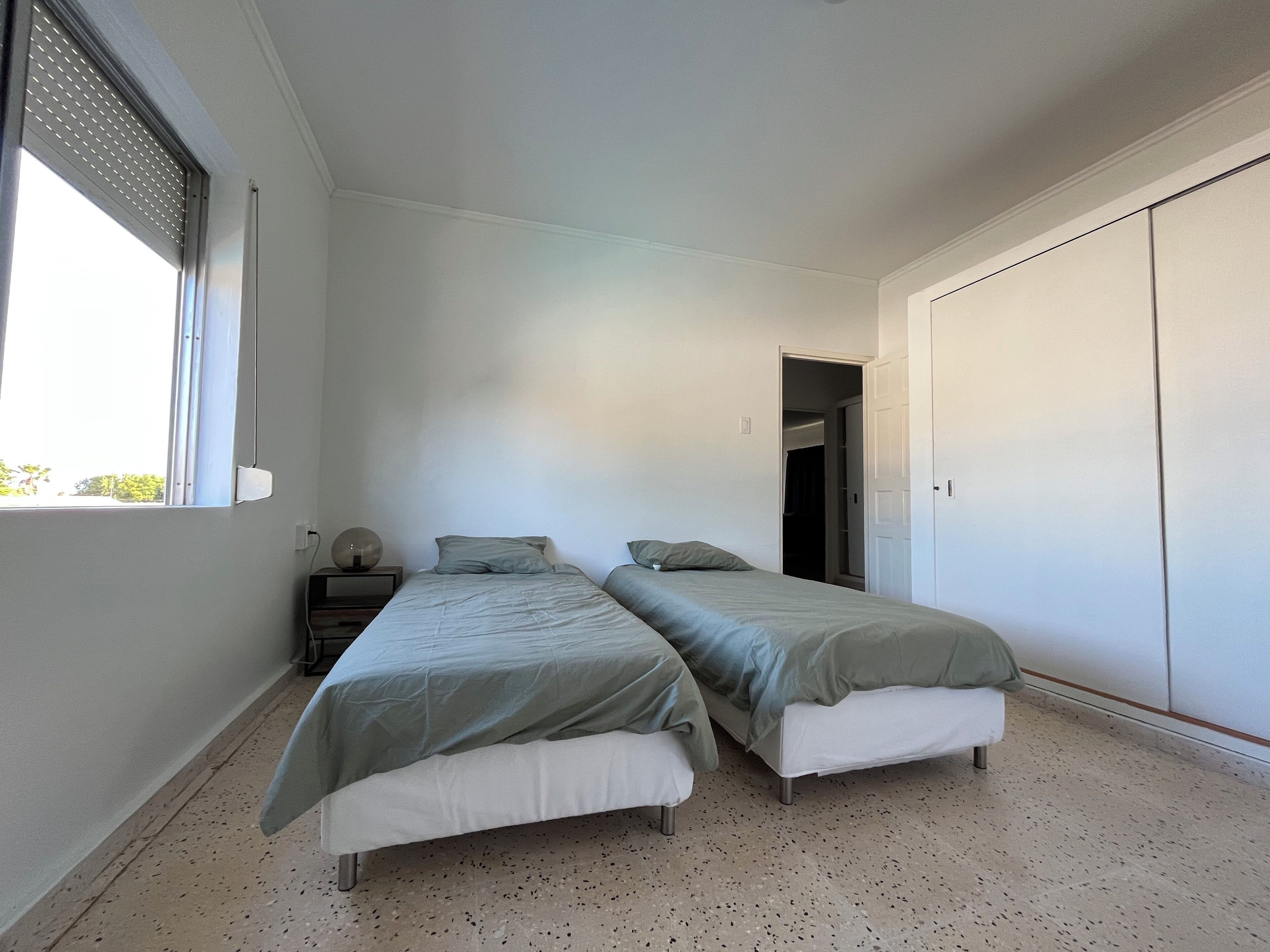 Un dormitorio con dos camas, un armario, una ventana y una puerta que da a otra habitación.