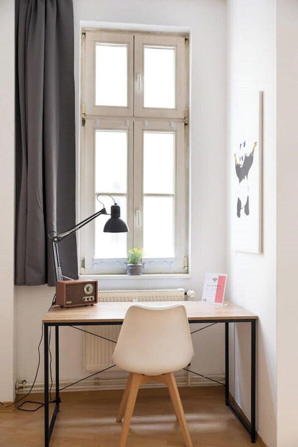 Une pièce comprenant un bureau, une chaise, une fenêtre avec des rideaux, un radiateur et une petite plante.