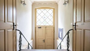 A hallway with a double door, a window with a diamond pattern, and a light fixture on the wall. - Ko-Living Space Opera | Suite 6 | Kitchen | Living room | Dart | City center (Halle (Saale))