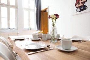Une table à manger dressée avec des assiettes, des tasses et des couverts, un vase rempli de fleurs et une fenêtre ornée de rideaux.