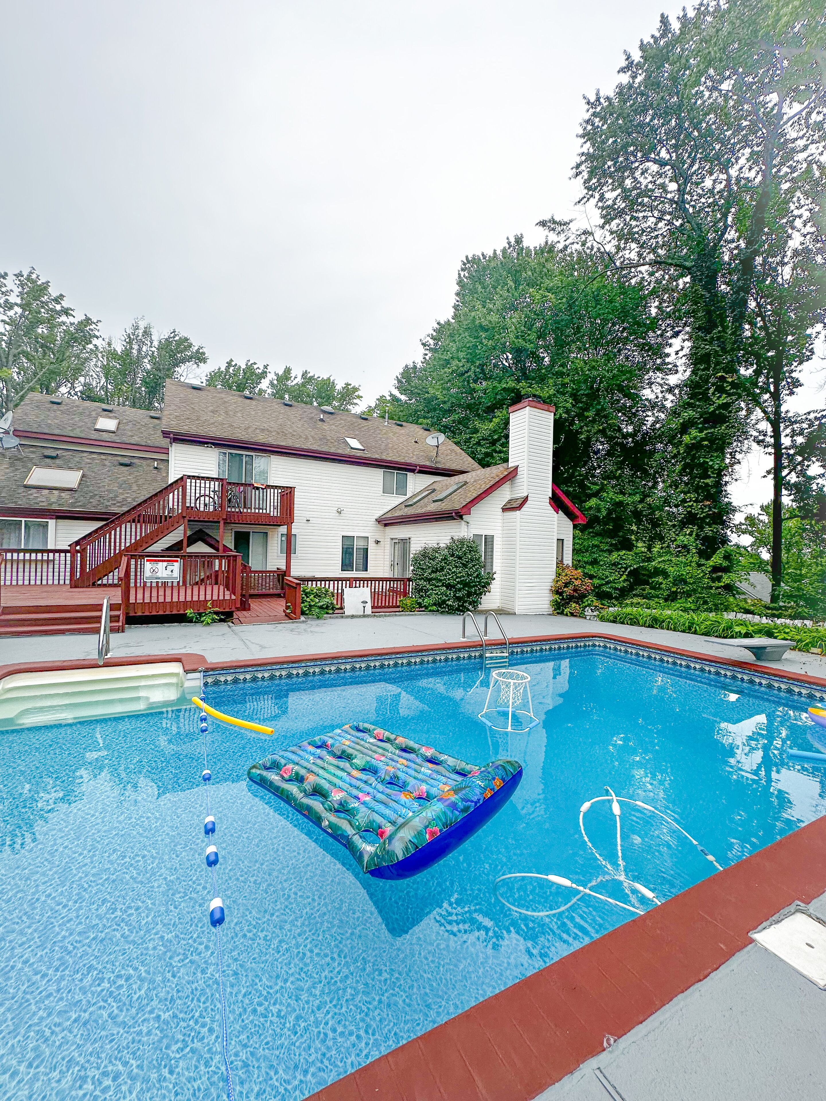 Une piscine résidentielle avec une terrasse rouge, un escalier en bois et une maison en arrière-plan.