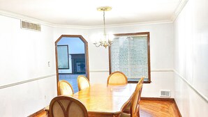 Ein Esszimmer mit Holztisch und Stühlen, einer Kristallleuchtre und einem Fenster mit Jalousien.