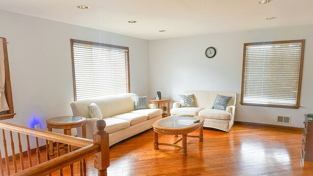 Ein geräumiges Wohnzimmer mit Holzboden, zwei Sofas, einem Couchtisch und großen Fenstern mit Jalousien.