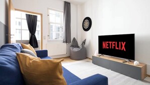 A modern living room with a blue sofa, a grey bean bag, a flat-screen TV displaying 'NETFLIX', and a dartboard on the wall. - ★ Ko-Living IX at the Opera | Right in the center | Free WiFi | Up to 4 people ★ (Halle (Saale))
