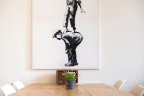 Uma área de refeições com mesa de madeira, cadeiras e uma obra de arte em preto e branco emoldurada na parede.