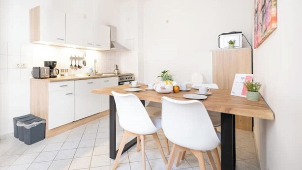 A modern kitchen with white cabinets, a wooden dining table, and two white chairs.