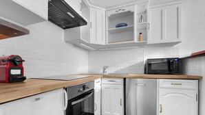 Une cuisine moderne avec des meubles blancs, un réfrigérateur en acier inoxydable, un four à micro-ondes et une machine à café rouge.