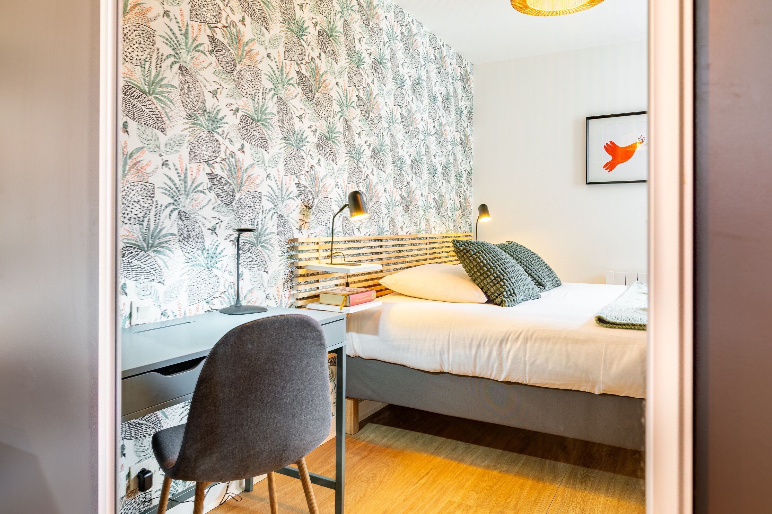 Un dormitorio con cama, escritorio, silla y una pared con estampado de piña.
