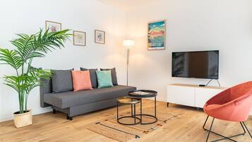 Un salon moderne avec un canapé gris, un fauteuil rouge, un téléviseur et une plante en pot.
