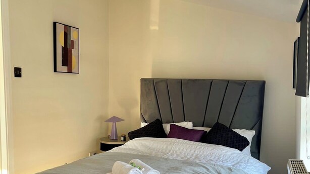 A neatly made bed with a grey headboard, white bedding, and rolled towels on the foot of the bed. - Trendy Apartment in The City - Shoreditch (London)