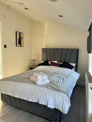 A neatly made bed with a grey headboard, white bedding, and rolled towels on the foot of the bed. - Trendy Apartment in The City - Shoreditch (London)