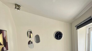 A modern living room with a grey sofa, a round glass coffee table, a potted plant, and a wall clock. - Trendy Apartment in The City - Shoreditch (London)