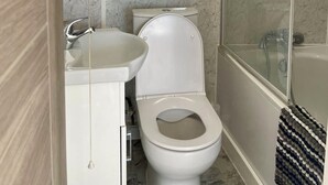 A bathroom with a marble wall, a toilet, a sink, and a shower. - Trendy Apartment in The City - Shoreditch (London)