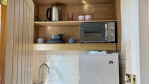 A compact kitchen with wooden cabinets, a stainless steel sink, a microwave, and a refrigerator. - Cosy En-suite in The City - Shoreditch (London)