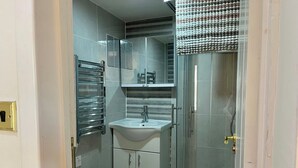A compact bathroom with a glass shower enclosure, a white sink, and a mirrored cabinet above it. - Cosy En-suite in The City - Shoreditch (London)