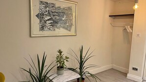 Una habitación con una mesa de mármol, dos plantas en macetas, una obra de arte abstracta enmarcada y un lámpara colgante.