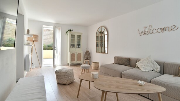 A modern living room with a sofa, ottoman, round coffee table, and a 'Welcome' sign on the wall.