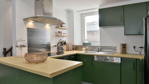A compact kitchen with green cabinets, a stainless steel range hood, and a wooden countertop.