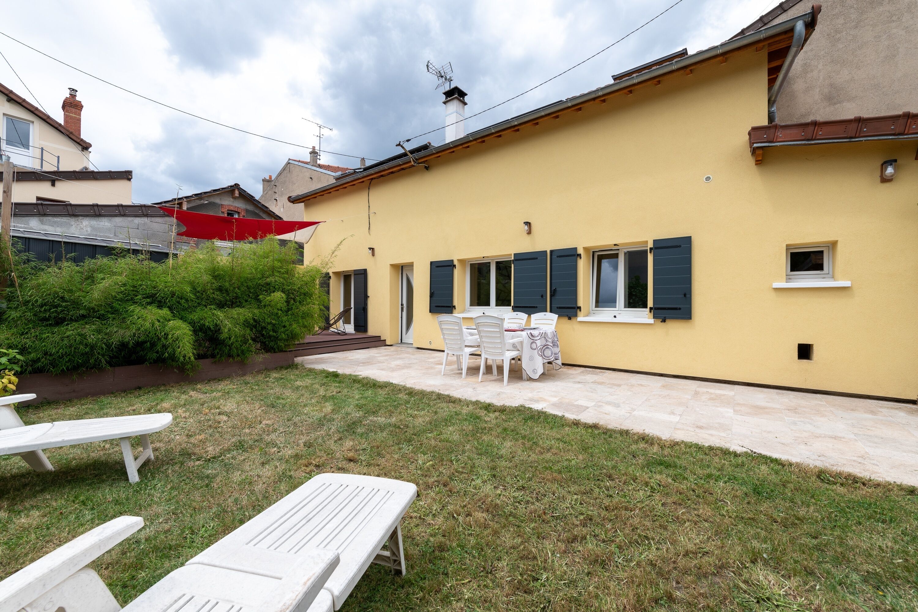 A yellow building with a patio area, outdoor seating, and a small garden.