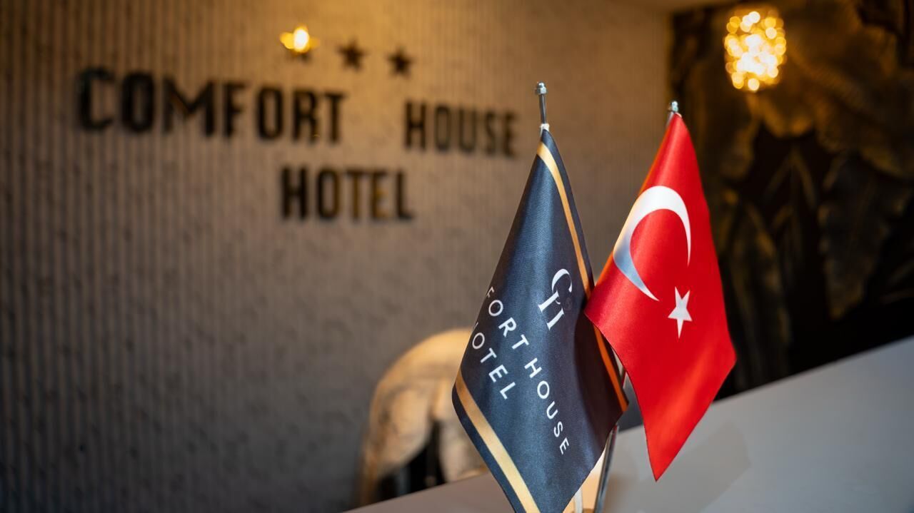 Flags of the Turkish Republic and the United Kingdom on a wall with the text 'COMFORT HOUSE HOTEL' above them.