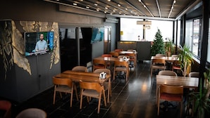 Un interior de restaurante moderno con mesas y sillas de madera, una pantalla de televisión y un árbol de Navidad.