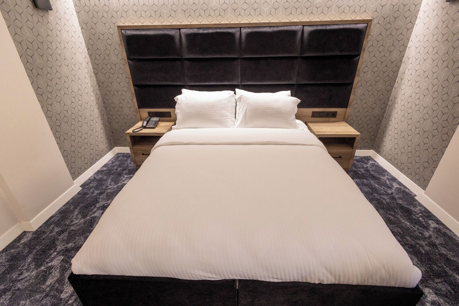 A hotel room with a large bed, two bedside tables, a telephone, and a patterned wall.