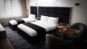 A hotel room with two beds, a round wooden table, a chair, and a nightstand with a lamp. - COMFORT HOUSE (Trabzon)