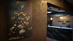 Un área de recepción con un cuadro de flores colgado en la pared y un letrero que dice 'COMFORT HOUSE HOTEL'.