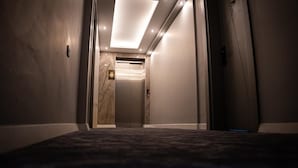 Un pasillo de hotel con piso alfombrado, pared de mármol y un ascensor.