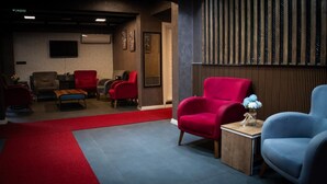 Un vestíbulo de hotel con alfombra roja, varias zonas de estar y un gran panel de madera.