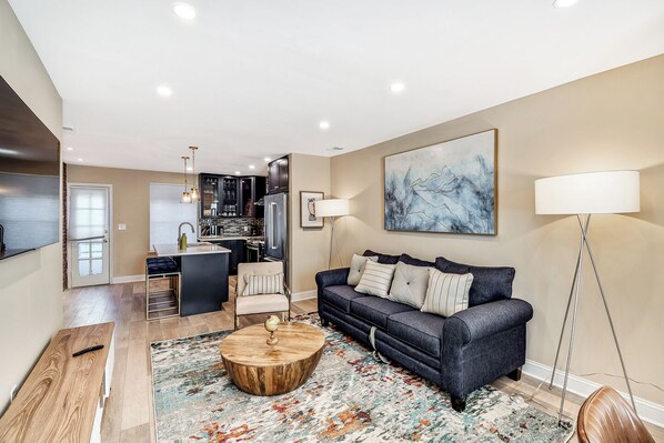 A modern living room with a dark blue sofa, a round wooden coffee table, and a colorful rug.