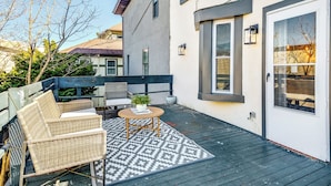 A deck with wicker furniture and a patterned rug, a white door, and a window with a view of trees. - Modern Downtown Retreat 5BR-5Baths (Philadelphia)