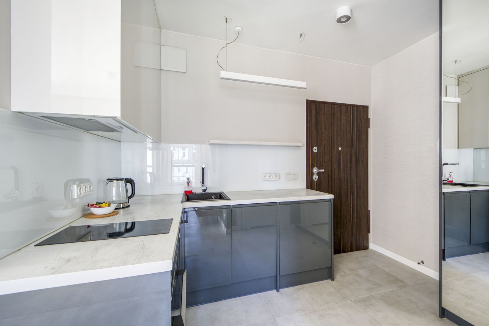 A modern kitchen with a central island, a built-in oven, and a dark wooden door.