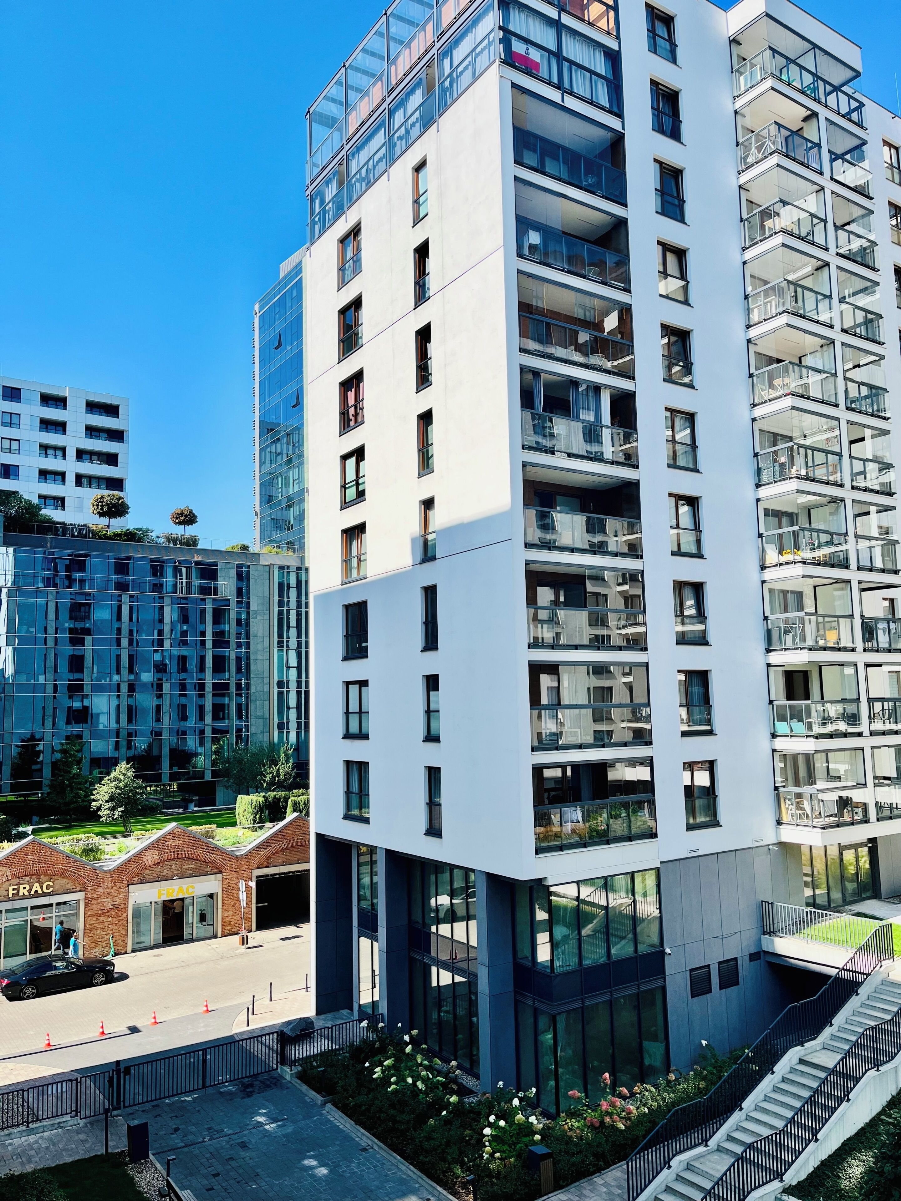 A modern multi-story building with a glass facade, multiple balconies, and a central courtyard with a staircase.