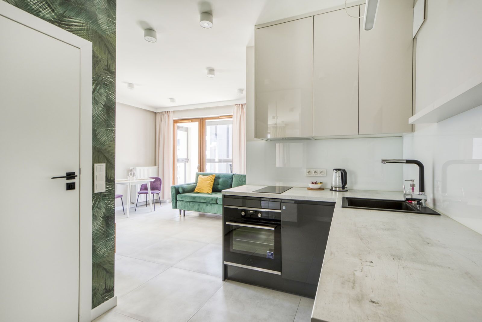 Eine moderne Küche mit integriertem Backofen, ein Essbereich mit Tisch und Stühlen und ein grünes Sofa im Wohnzimmer.