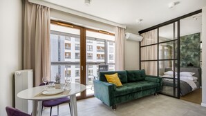 Una sala de estar moderna con un sofá verde, una mesa de comedor con sillas y un ventanal con cortinas.